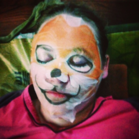 Shows someone relaxing at a jjimjilbang with a sheet mask on.